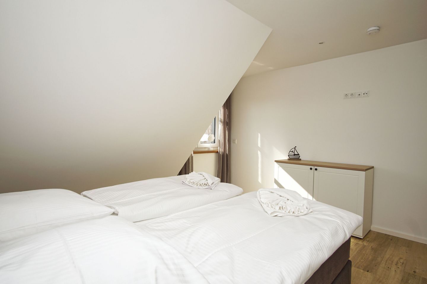 A bedroom with two beds, a wooden headboard, a bedside table, and a window with curtains.