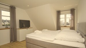 A bedroom with a bed, a television on a stand, and a window with curtains. - Strandhaus Anni - comfortable and modern vacation home - Strandhaus Anni (Mönchgut)