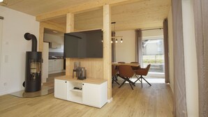 A modern living room with a wooden ceiling, a TV mounted on a wooden wall, a fireplace, and a dining area with chairs. - Strandhaus Anni - comfortable and modern vacation home - Strandhaus Anni (Mönchgut)
