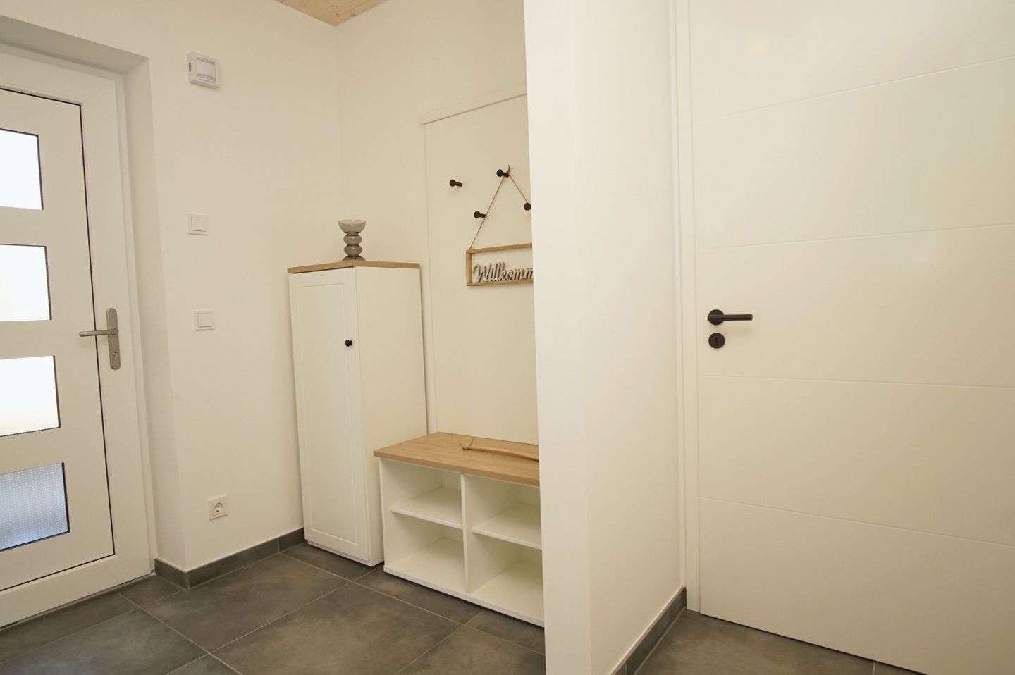 A hallway with a white door, a white wardrobe, a small wooden table, and a wall-mounted sign.