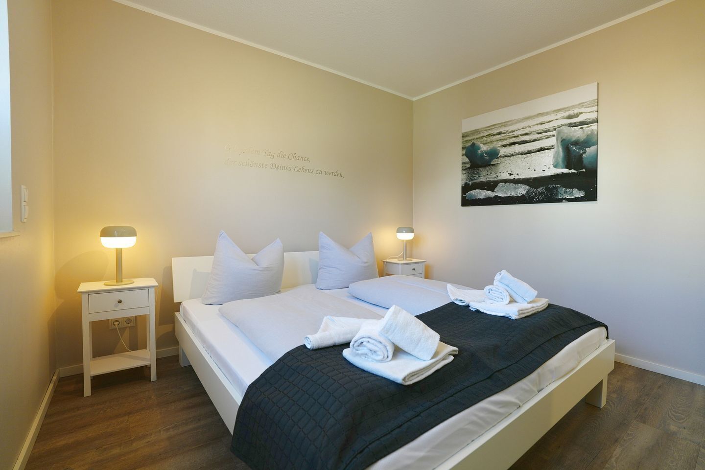 Hotelkamer met een bed, twee nachtkastjes, een kunstwerk aan de muur en een opgemaakt bed met handdoeken.