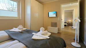 Ett hotellrum med en säng, en tv, ett litet sidobord, en stol och en rymlig klädkammare.