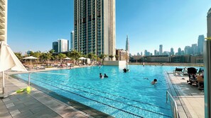 A swimming pool with clear water, surrounded by lounge chairs and umbrellas, with tall buildings in the background. - Luxury Stays @ Downtown Views 2 with UniDwellers Holiday Homes (Dubai)