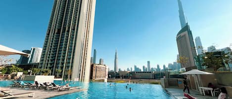 Une piscine entourée de chaises longues, bordée d’immeubles de grande hauteur et surplombant un ciel dégagé.