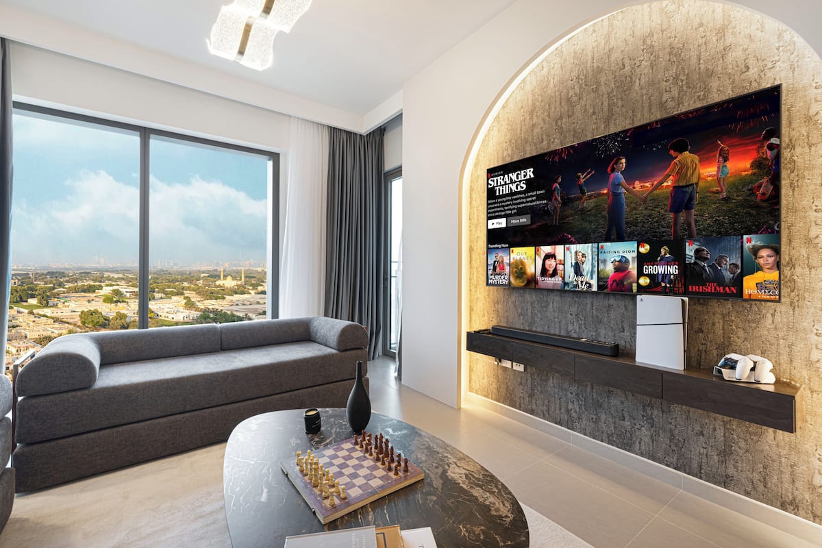 Una sala de estar moderna con un televisor grande, un sofá, una mesa de centro con un tablero de ajedrez y vistas a la ciudad.