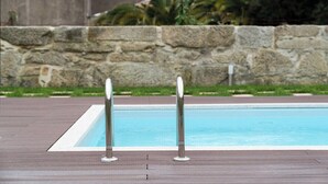Piscina com dois postes de segurança metálicos e um muro de pedra ao fundo.