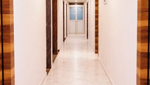 Um corredor com piso de mármore, painéis de madeira nas paredes e uma porta dupla no final.