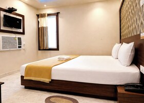 Habitación de hotel con cama, televisor, aire acondicionado, ventana con cortinas y teléfono junto a la cama.