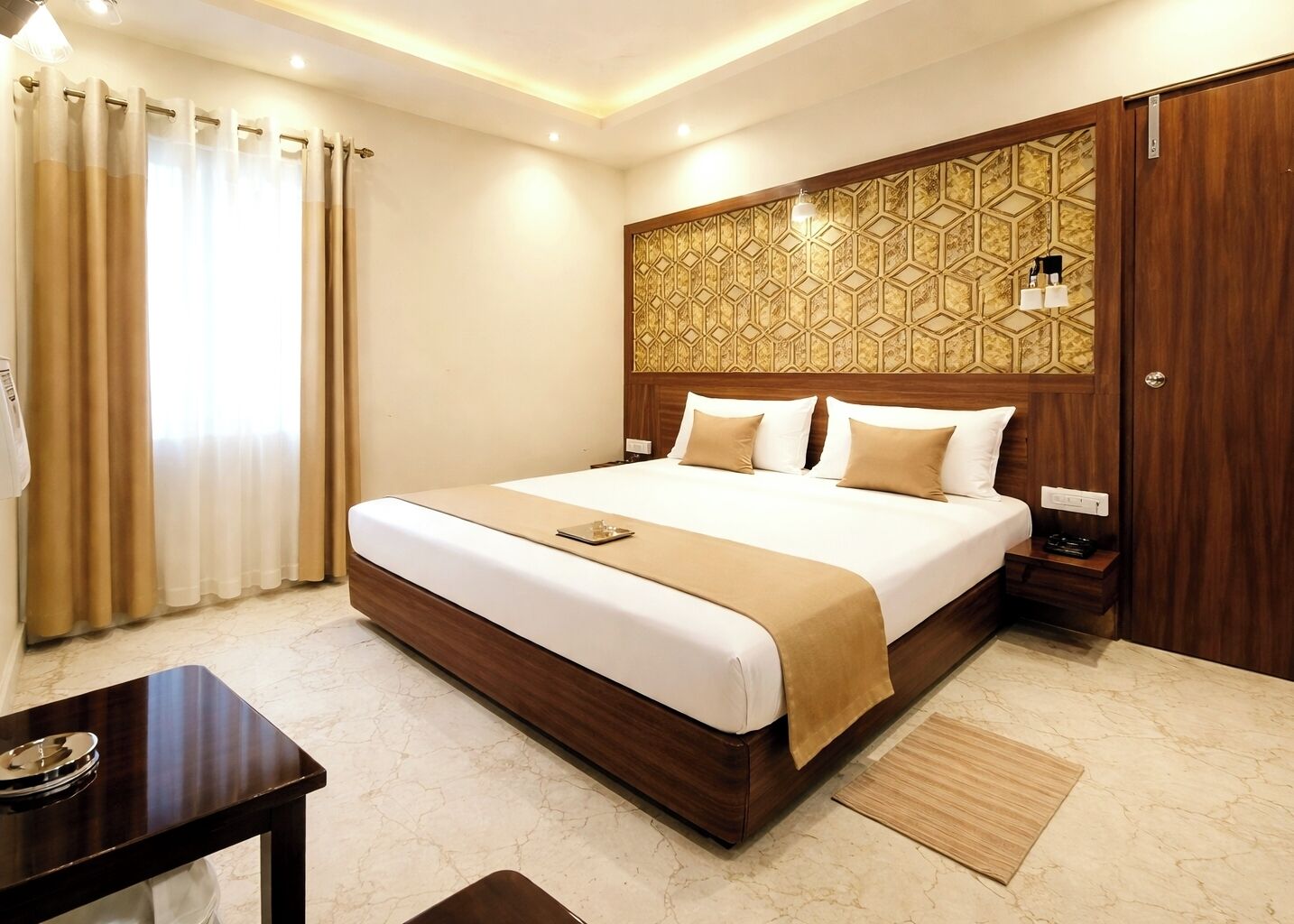 A hotel room with a large bed, a bedside table, a desk, and a patterned headboard.