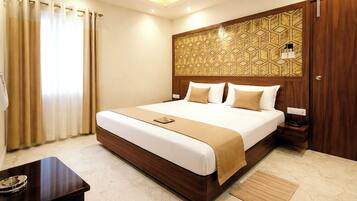 A hotel room with a large bed, a bedside table, a desk, and a patterned headboard.
