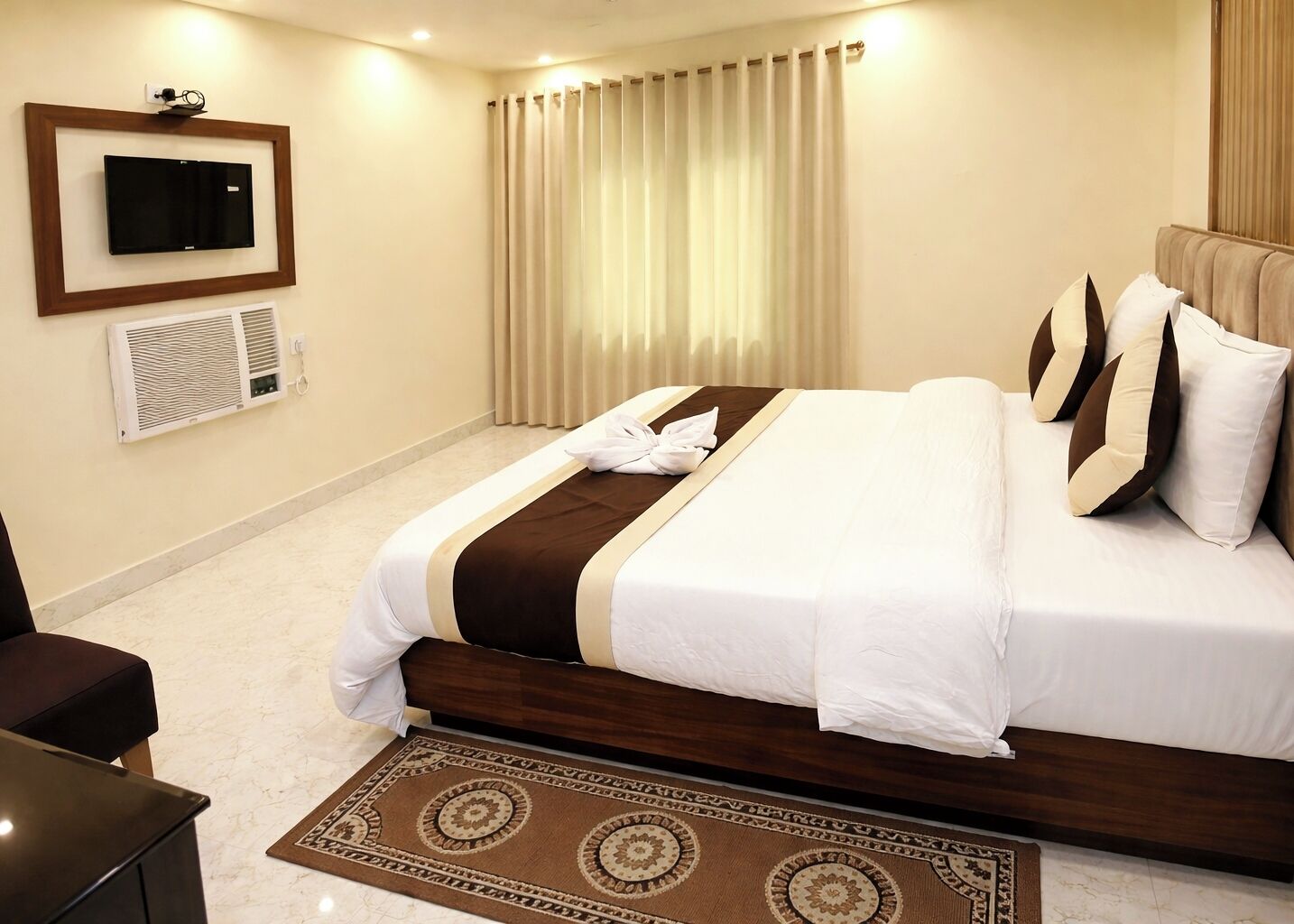 A hotel room with a bed, a TV, curtains, and a carpet.