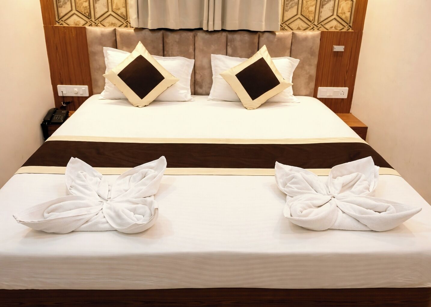 A neatly made bed with a brown headboard, white bedding, and two towels arranged on the bed.