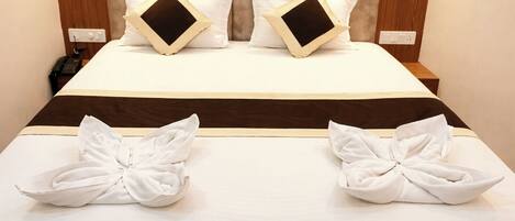 A neatly made bed with a brown headboard, white bedding, and two towels arranged on the bed.
