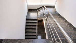 Escadaria moderna com corrimão de metal, claraboia acima e piso de mármore escuro.