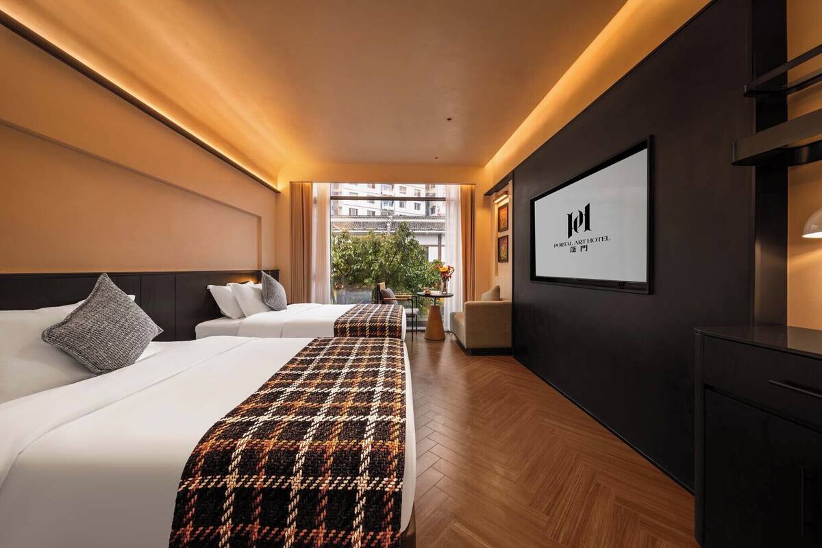 Une chambre d’hôtel avec deux lits, une grande fenêtre, un panneau encadré accroché au mur et une vue sur les bâtiments environnants.