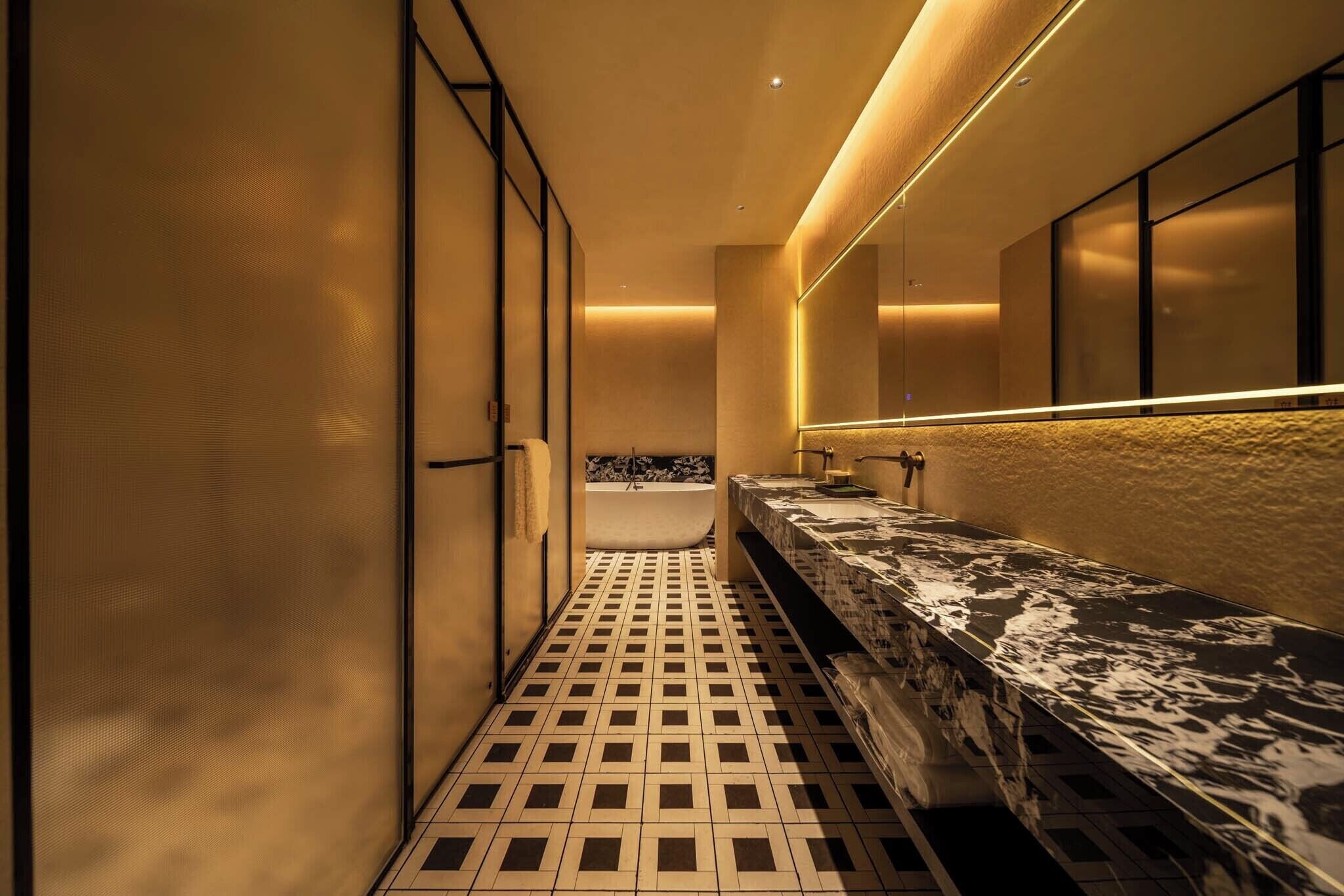 A modern bathroom with a tiled floor, a bathtub, and a long counter with a mirror.