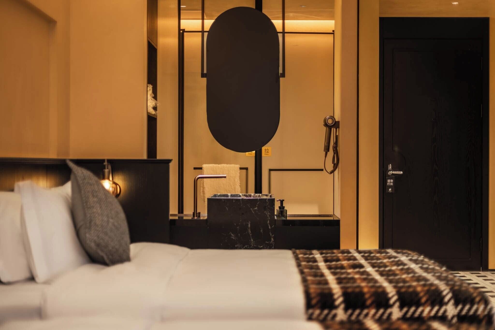 Une chambre d’hôtel avec un lit, un grand miroir, une table d’appoint en marbre noir, un lavabo et une porte.