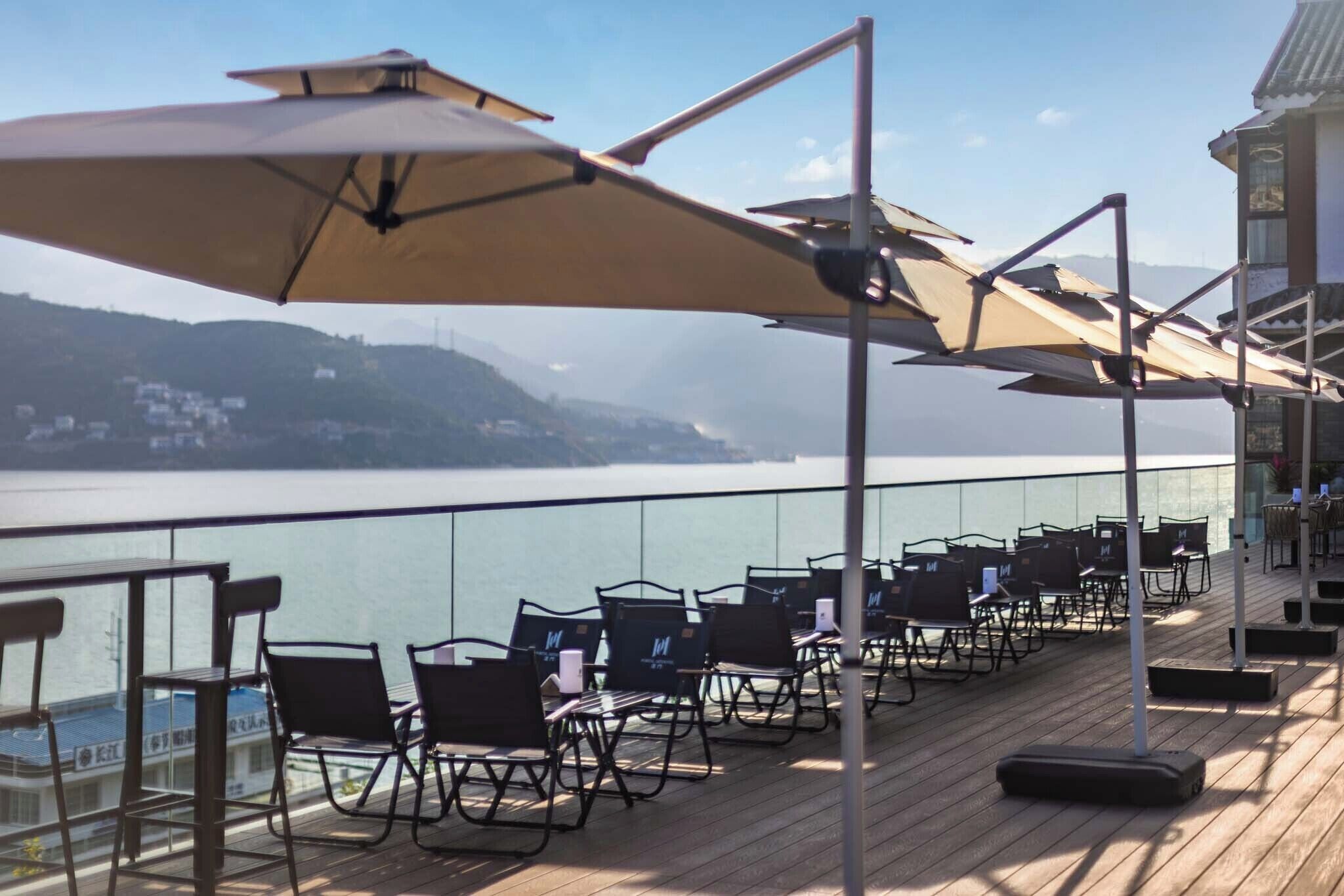 Een terras met buiten zitplaatsen, parasols en uitzicht op water en heuvels.