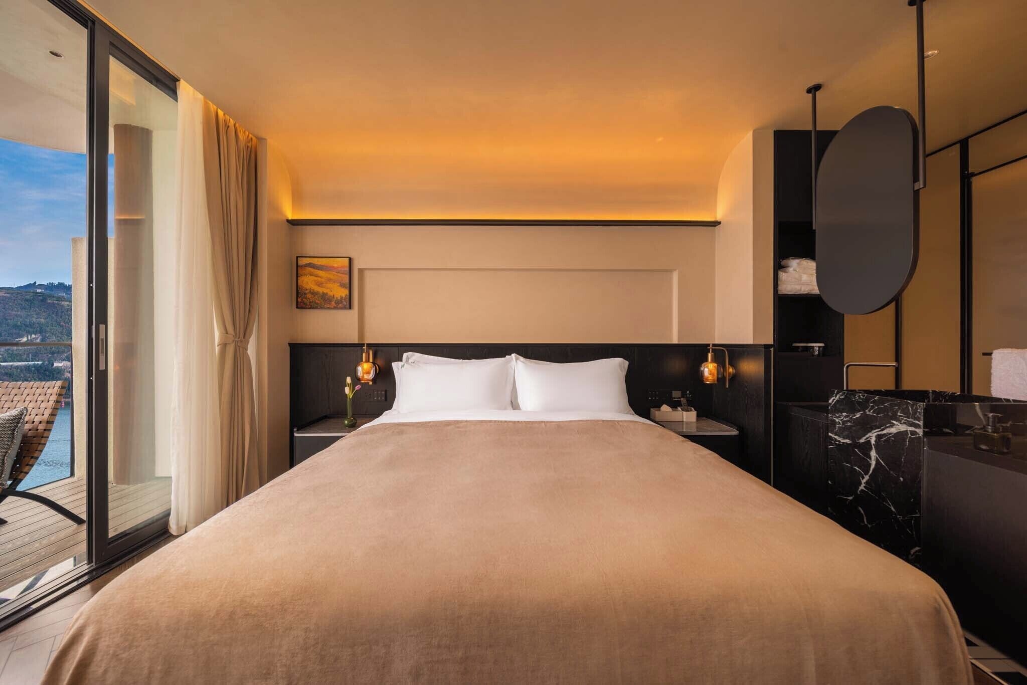 Habitación de hotel con una cama grande, una mesita de noche con lámpara, un baño con encimera de mármol y vistas al exterior.