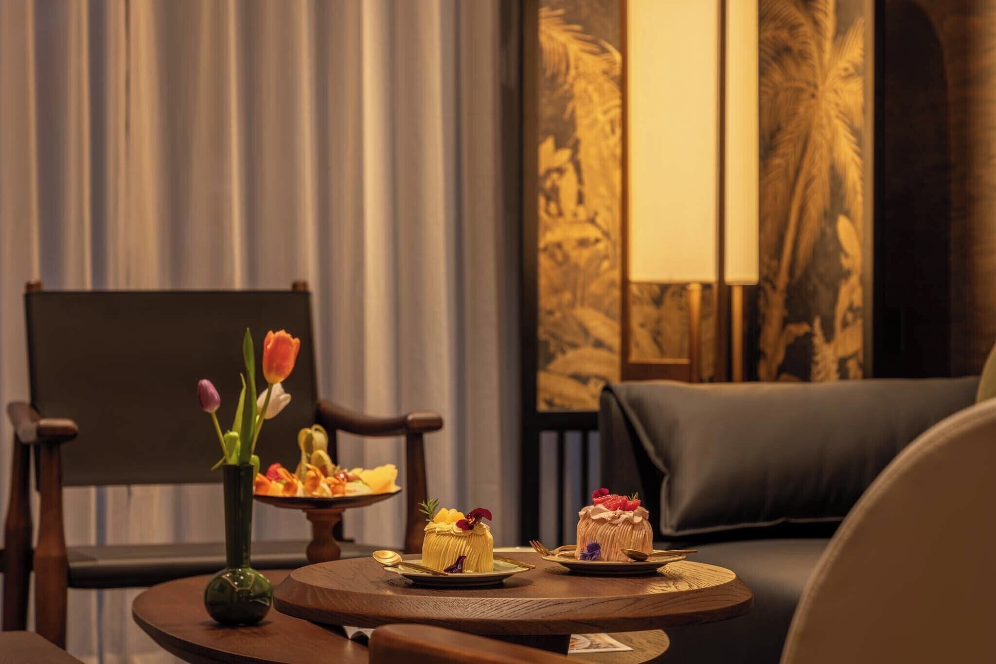 A room with a round table, a vase with flowers, and a chair.