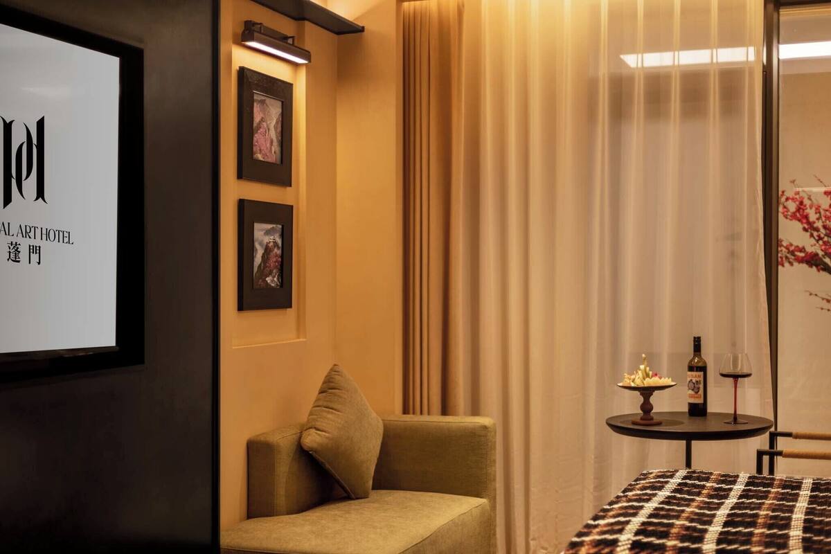 Une chambre d’hôtel avec un canapé, une petite table sur laquelle se trouvent une bouteille et un verre, et des tableaux encadrés accrochés au mur.