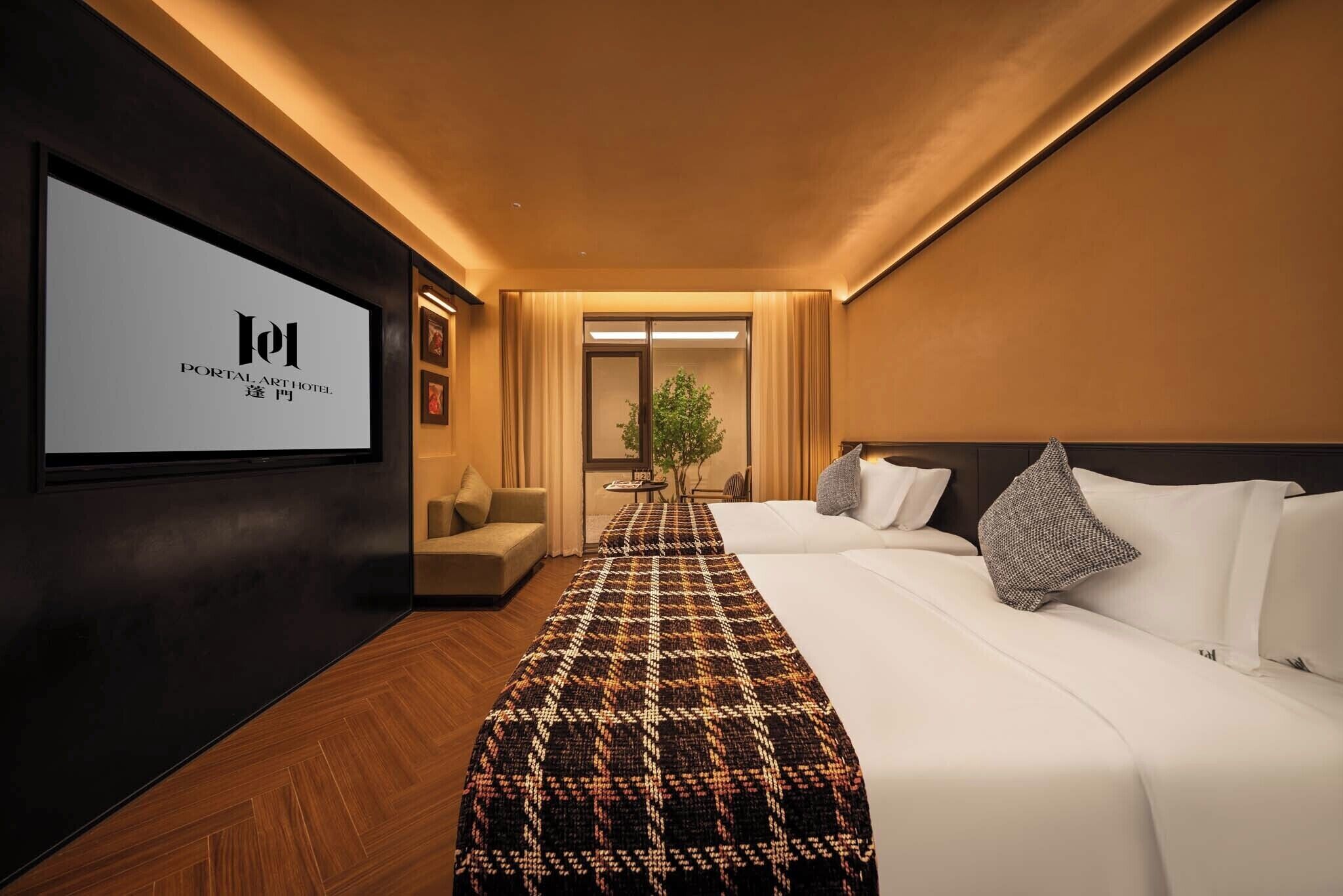 A hotel room with a bed, a TV screen displaying the hotel name, a sofa, and a small table with a plant.