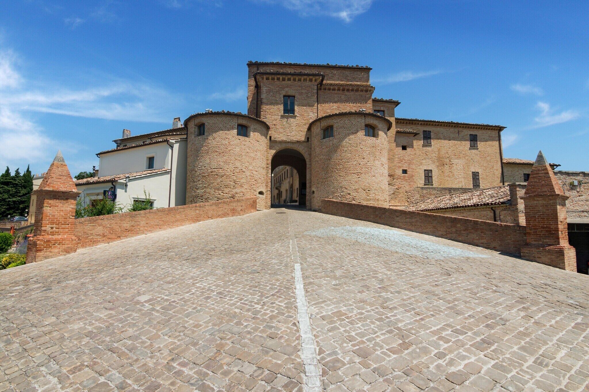 A historic building with a central archway, brick walls, and a paved courtyard.