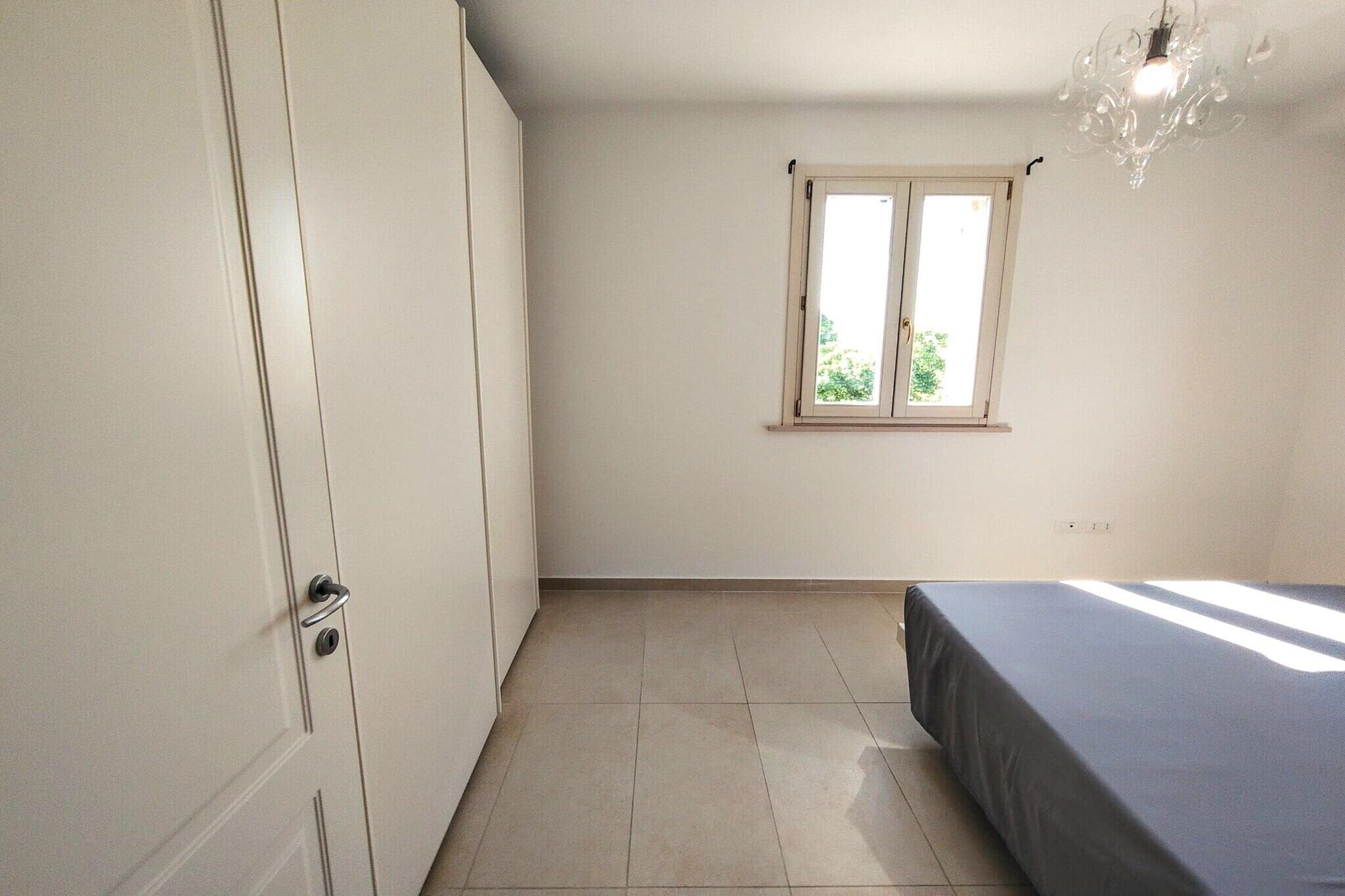 A room with a bed, a window, a door, and a chandelier.