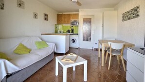 Ein kompakter Wohnraum mit einer Couch, einem kleinen Tisch, einer Essecke mit Stühlen, einer Küche mit Mikrowelle und einer Waschmaschine.