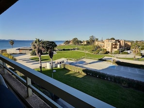 A coastal view with a paved area, palm trees, and buildings in the background. - One-bedroom apartment with a sleeping nook, air conditioning, and a view of the sea (La Londe-les-Maures)