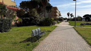 Ein gepflasterter Weg mit einer Bank, umgeben von Grünflächen und Gebäuden.
