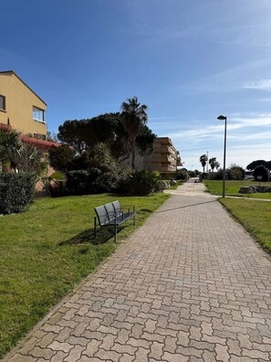 A paved pathway with a bench, surrounded by greenery and buildings. - One-bedroom apartment with a sleeping nook, air conditioning, and a view of the sea (La Londe-les-Maures)