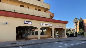 Ein Gebäude mit den Schildern 'Proxi' und 'Coiffure', einem überdachten Eingang und blauem Himmel.