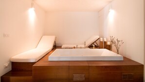 Un bagno moderno con una vasca da bagno ampia, due poltrone bianche imbottite e un mobile contenitore in legno.