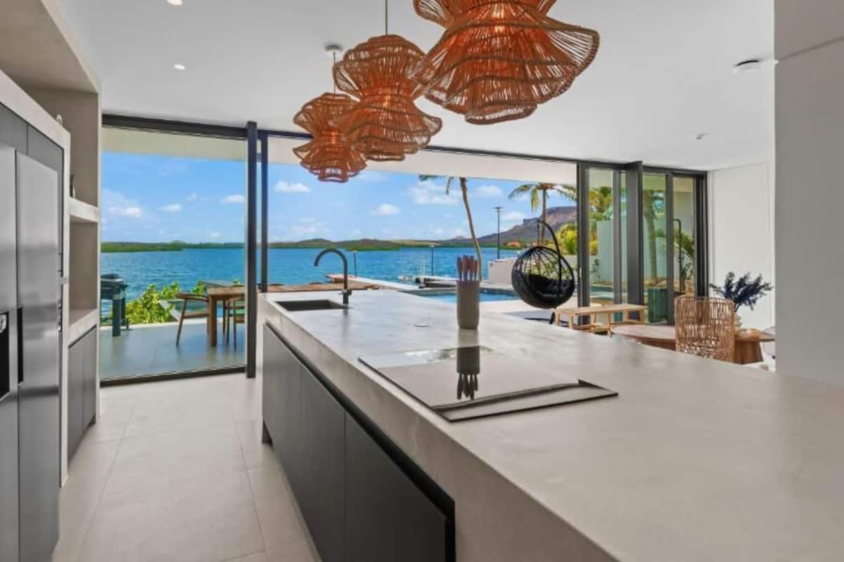 Una cucina moderna con una grande isola, vista sul mare e zona pranzo con posti a sedere all'aperto.