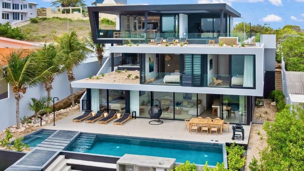 Una casa moderna de dos pisos con piscina, mobiliario exterior y vistas del paisaje circundante.