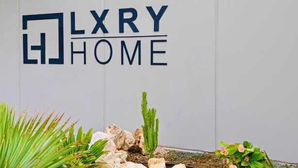 A sign for 'LXRY HOME' with a minimalist design, featuring a cactus and some greenery in front. - Villa Wave (Willemstad)