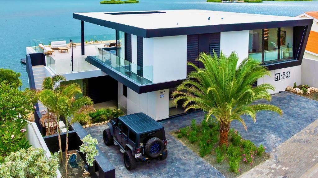 Una casa moderna con balcón de cristal, garaje y entrada para vehículos.