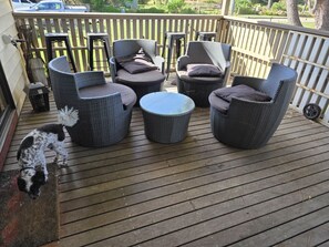 Eine Holzterrasse mit Korbmöbeln, darunter Stühle und ein runder Tisch.