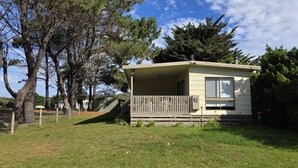 A small, single-story mobile home with a porch, surrounded by grass and trees. - Where Paris meets Jupiter - Linen, Wi-Fi, Pets OK (Venus Bay)