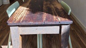 A dining area with a rustic wooden table, light green chairs, and a framed picture of a beach scene on the wall. - Where Paris meets Jupiter - Linen, Wi-Fi, Pets OK (Venus Bay)