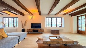 A spacious living room with exposed wooden beams, a large flat-screen TV, a sofa, a coffee table, and large windows. - Luxury Villa with Garden & Zipline (La Roche-en-Ardenne)