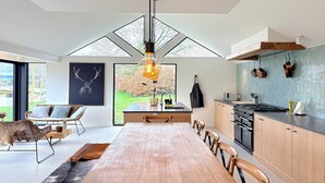 A modern kitchen with a dining area, large windows, and a hanging light fixture. - Luxury Villa with Garden & Zipline (La Roche-en-Ardenne)