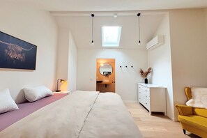 Een slaapkamer met een bed, nachtkastje, lamp, spiegel, kaptafel en een gele fauteuil.
