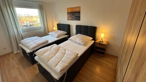A hotel room with two beds, a window with curtains, a painting on the wall, and a nightstand with a lamp. - behagliche Ferienwohnung in Elstra (Elstra)