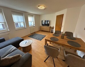 Ein modernes Wohnzimmer mit einer Couch, einem Couchtisch, einem Esstisch mit Stühlen, einem Fernseher und einer Heizung.