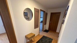 A hallway with wooden flooring, a small wooden table, a black rug, a round mirror, and a wooden door. - behagliche Ferienwohnung in Elstra (Elstra)