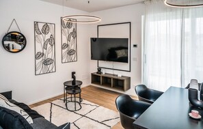 A modern living room with a flat-screen TV, black and white artwork, a round table, and a dining area with chairs. - Art&Fashion- Ariom Apartments (Moniga del Garda)