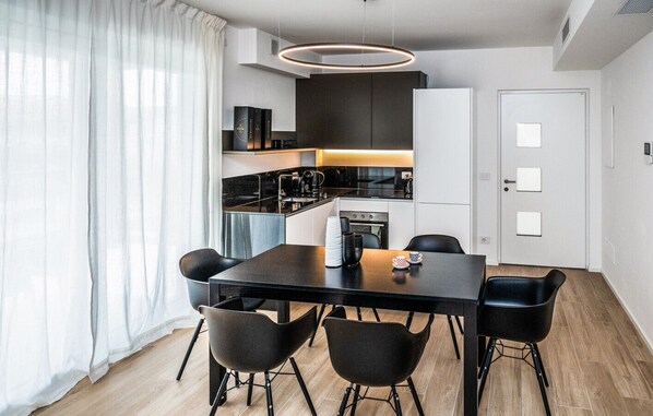A modern kitchen with a dining area, including a table and chairs, a coffee machine, and a built-in oven. - Art&Fashion- Ariom Apartments (Moniga del Garda)