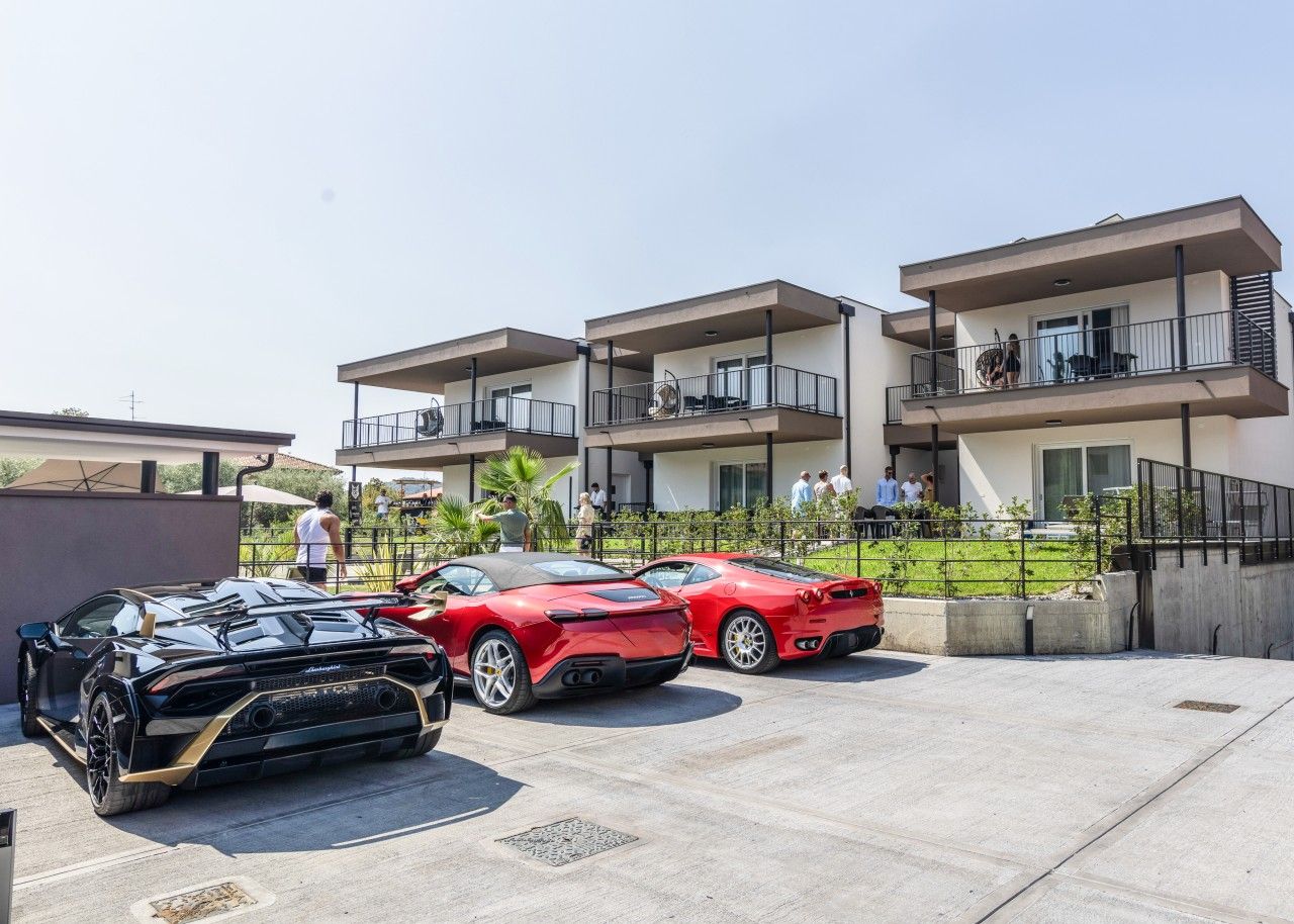 A parking area with three sports cars, a modern building with balconies, and a clear sky.